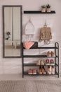 Black shelving unit with shoes and different accessories near white wall in hall. Storage idea