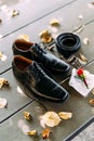 Black shoes of a man with untied laces on a wooden texture with a belt and groom`s boutonniere on a white pocket square.