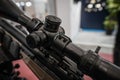 Black shooting scope optics mounted on rifle displayed at weapons exhibition fair, closeup detail to adjustment knobs