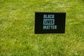 Black sign with blue writing on a green grass lawn that says black lives matter