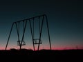 Black silhouettes of a couple of metal abandoned empty swings at dusk Royalty Free Stock Photo