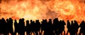 black silhouettes of many people against the background of a solid wall of fire