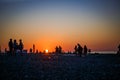 Black silhouettes of people on the beach in the sunset light of the orange sun.