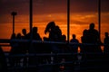 Black silhouettes of people on the waterfront in the orange light of sunset.