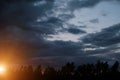 Black silhouettes trees, storm clouds with light breaking through from sun at sunset