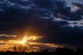 Black silhouettes trees, storm clouds with light breaking through from sun at sunset