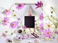 Black sketchbook on a wooden easel, scattered pencils and pens, strewn pink flowers and steaming coffee white cup. Royalty Free Stock Photo