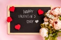 A black slate with the words `Happy Valentine`s day` on it. Romantic pink background with flowers and hearts. Royalty Free Stock Photo