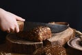 Black sliced bread on the board, vintage knife, female hand than slicing bread on the table and a wooden background on a stump, co Royalty Free Stock Photo