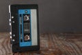 A black, slightly dusty Maxell audio cassette stands edge-on against a brown wooden background