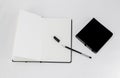 Black small closed square notepad and large open notebook with blank white pages and ballpoint pen with cap on white back Royalty Free Stock Photo