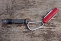 A black small flashlight and a red folding knife on a gray iron carabiner latch Royalty Free Stock Photo