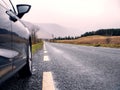 Black small rented car parked off small asphalt road. Mountains in the background. Irish nature landscape. Nobody. Travel and