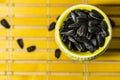 Black small sunflower seeds. Click seeds with husks. A handful in a yellow miniature stand on a wooden napkin. Spilled some seeds.