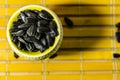 Black small sunflower seeds. Click seeds with husks. A handful in a yellow miniature stand on a wooden napkin. Spilled some seeds.