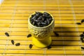 Black small sunflower seeds. Click seeds with husks. A handful in a yellow miniature stand on a wooden napkin. Spilled some seeds.