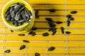 Black small sunflower seeds. Click seeds with husks. A handful in a yellow miniature stand on a wooden napkin. Spilled some seeds.