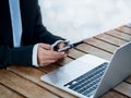 Black smart mobile phone in business woman`s hand in suit who holding and using near the notebook computer on desk. Royalty Free Stock Photo