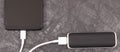 Black smartphone with connected plug of external powerbank. Mobile phone charging. Place for text