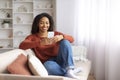 Black smiling woman in casual wear using her smartphone at home Royalty Free Stock Photo