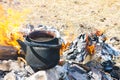 A black smoked teapot stands on fire surrounded by yellow flame tongues against the background of dry grass - tourist inventory