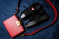 Black sneakers with red tongues and a red bag with a golden lock on a blue woven background