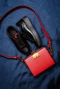 Black sneakers with red tongues and a red bag with a golden lock on a blue woven background