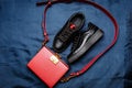 Black sneakers with red tongues and a red bag with a golden lock on a blue woven background