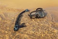Black snorkel breathing tube and diving mask, in shallow sea on fine sand beach, sun shining on clear water