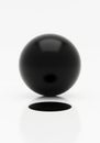 A black sphere levitates above a white surface, casting a shadow directly beneath it. The sphere\'s Royalty Free Stock Photo
