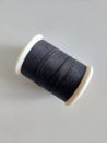 Black spool of sewing thread on white table.