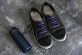 Black sports sneakers with two-tone laces along with a blue plastic container with water on a gray surface Royalty Free Stock Photo