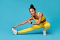 Black sportswoman in yellow fitwear stretching legs against blue background Royalty Free Stock Photo