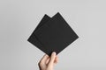 Black Square Flyer / Invitation Mock-Up - Male hands holding black flyers on a gray background Royalty Free Stock Photo