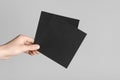 Black Square Flyer / Invitation Mock-Up - Male hands holding black flyers on a gray background Royalty Free Stock Photo