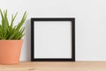 Black square frame mockup with a aloe vera in a ceramic pot on a wooden table Royalty Free Stock Photo