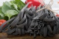Black squid ink tinted tagliatelle pasta, uncooked, with basil and tomatoes in the background, on a wooden board Royalty Free Stock Photo