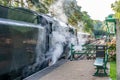 Traditional steam train at a train station releasing pressure and smoke