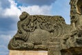 Black stone beam with damaged sculpture of man on beast with open mouth against at Brahma Jinalaya temple.