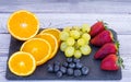 Black stone cutting board with mix of fresh seasonal fruit. Grape, strawberry, blueberry and oranges. Light and healthy snack