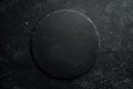 Black stone round slate plate on a black stone background. Top view. Free space for your text