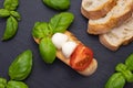 On a black stone stand are crackers with a small mozzarella, basil and chopped tomatoes and other croutons