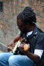 Black street musician sits against wall plays guitar London England