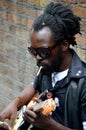 Black street musician sits against wall plays guitar London England