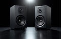 Black studio speakers placed on a reflective surface under a focused spotlight Royalty Free Stock Photo
