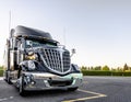 Black stylish big rig semi truck with bright chrome grille stand on wide parking lot Royalty Free Stock Photo