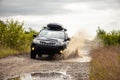 Black Subaru Forester driving on a dirt road with puddles