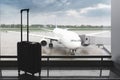 A black suitcase stands in an airport building amid a loading airplane