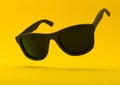 Black summer sunglasses falling down on a pastel bright yellow background Royalty Free Stock Photo