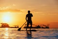 Black sunset silhouette of paddle boarder standing on SUP